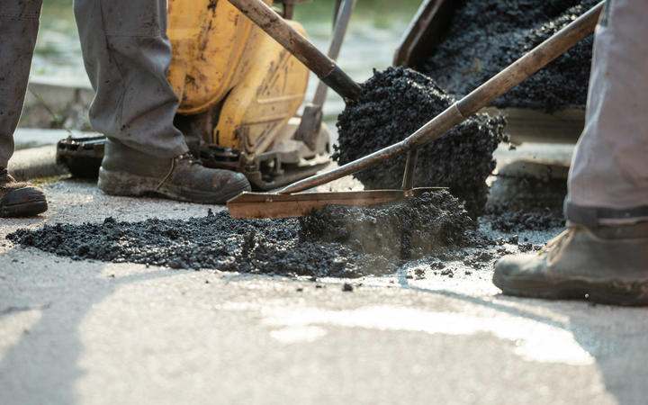 Two construction workers working together to patch a bump in the road with fresh asphalt.