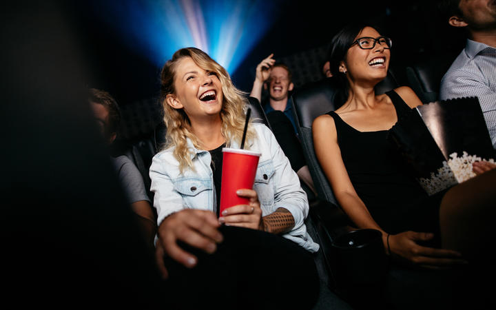Young people laughing while watching film in movie theater.