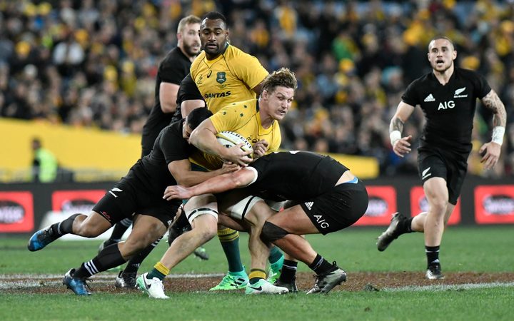 Wallabies captain Michael Hooper is wrapped up by the All Blacks