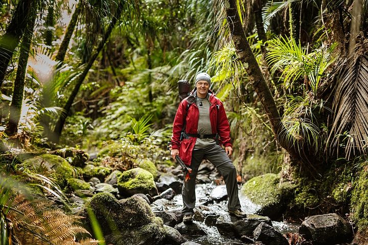 A landscape portrait of Bruce Hopkins wearing tramping clothes and standing in a rain forest.