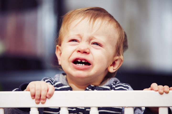 A photo of a little boy is standing in his cot crying