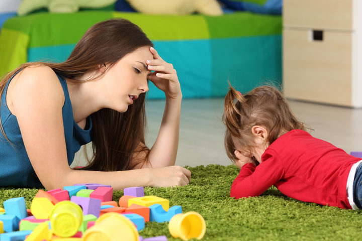 A photo of a frustrated crying baby and a tired mother with some toy blocks lying near them