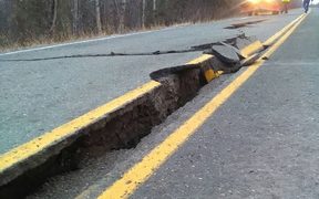 People walk past a crack in the road after an earthquake near Northwoods on the Kenai Spur Highway in Kenai, Alaska