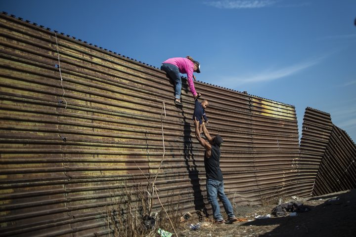 A group of Central American migrants climb the border fence between Mexico and the United States, near El Chaparral border crossing, in Tijuana, Baja California State, Mexico.