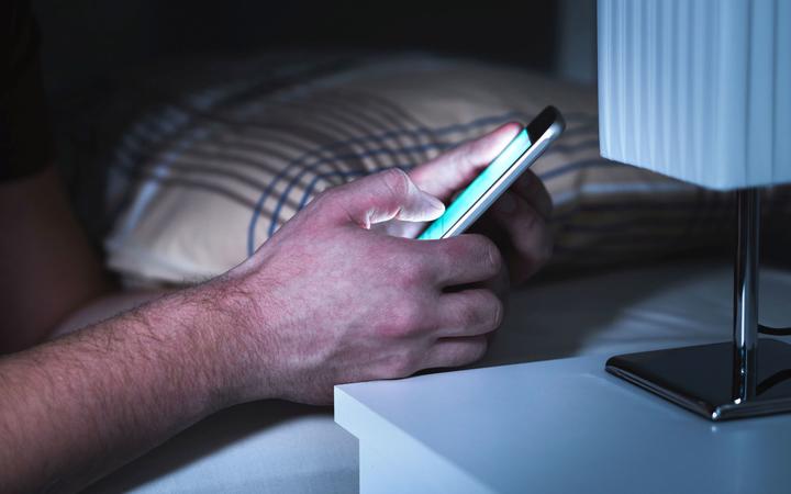 Man using smartphone in bed late, in the middle of the night. Mobile phone in bedroom. Texting or using social media. Cellphone addiction.
