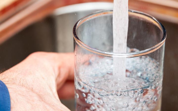 Closeup shot of a man pouring a glass of fresh water from a kitchen faucet