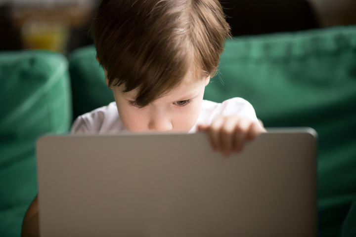 A photo of a Curious interested kid boy secretly looking watching forbidden censored adult only internet online video content on laptop alone, parental protection, computer control and security for child concept