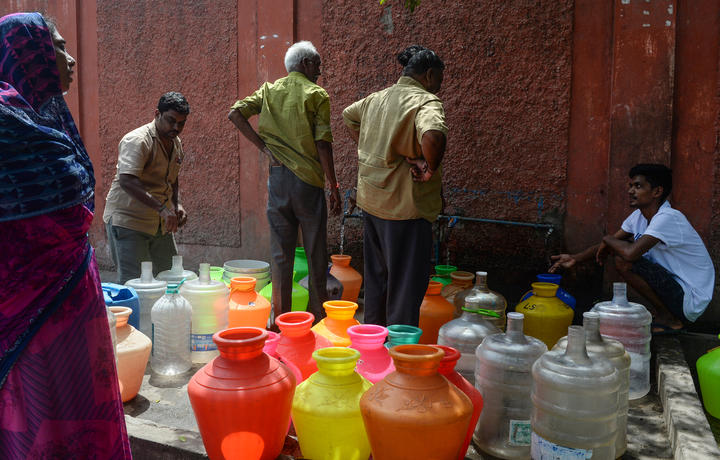 Indian residents stand around with plastic pots filled with drinking water at a distribution point in Chennai on June 19, 2019.
