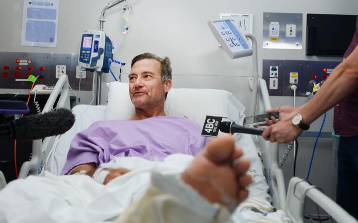 This handout photo received from Princess Alexandra Hospital in Brisbane on September 18, 2019 shows Neil Parker, 54, an Australian bushwalker talking to the media from his hospital bed after he tumbled down a waterfall, snapping his leg in two