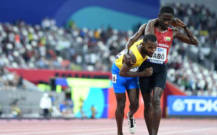 Guinea-Bissau's Braima Suncar Dabo (R) helps Aruba's Jonathan Busby to the finish line during the Men's 5000m heats at the 2019 IAAF World Athletics Championships at the Khalifa International stadium in Doha on September 27, 2019. (Photo by Kirill KUDRYAVTSEV / AFP)