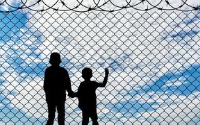 Refugee children concept. Silhouette of two children of refugees near the border fence of barbed wire