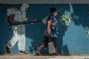 A woman walks past graffiti in Rio de Janeiro depicting a man performing a disinfection and the face of President Jair Bolsonaro represented by a virus. 