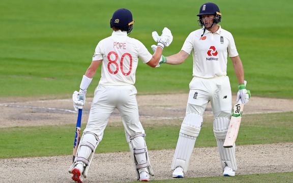 England's Ollie Pope (L) congratulates England's Jos Buttler (R) on reaching 50 during play on the first day of the third Test cricket match between England and the West Indies at Old Trafford in Manchester, north-west England on July 24, 2020.