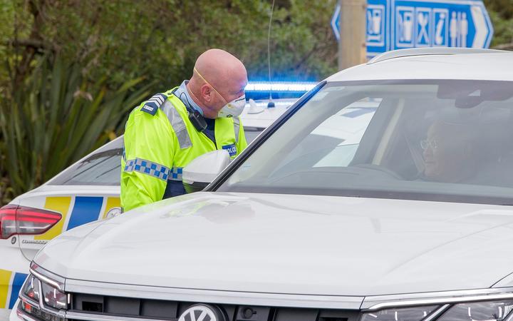 A police officer speaks to a driver wanting to leave the city at a COVID-19 check point setup at the southern boundary in Auckland on August 14, 2020. 