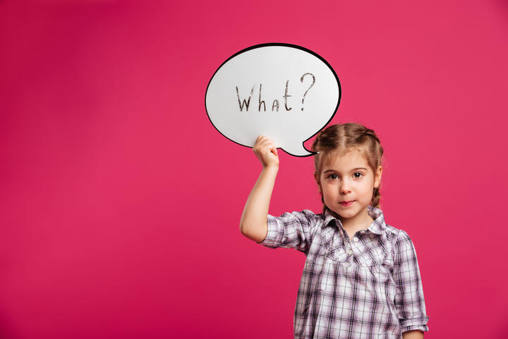 Image of pretty little girl child standing isolated over pink background. Looking camera holding speech bubble.
