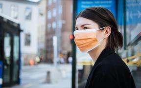 A young woman wearing a face mask at a bus stop.