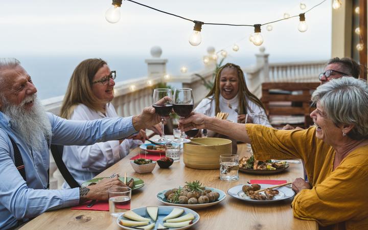 Multiracial senior friends having fun dining together and toasting with red wine on house patio dinner - Food and holidays concept