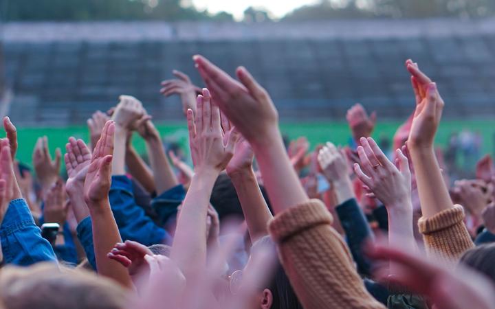Audiencia con las manos levantadas en un festival de música y luces cayendo desde arriba del escenario.