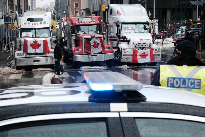 人们走在加拿大议会大楼附近，数百名卡车司机及其支持者聚集在渥太华市中心的街道上，作为卡车抗议者车队的一部分，他们反对 Covid 的命令。