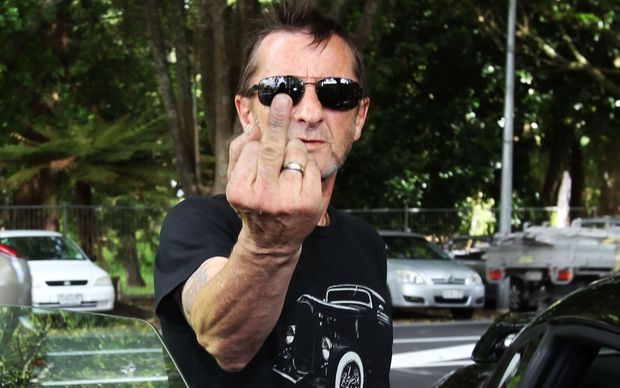 Phil Rudd gestures to media as he leaves court.