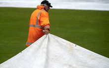 A groundsman pulls the covers as rain falls during a cricket game.