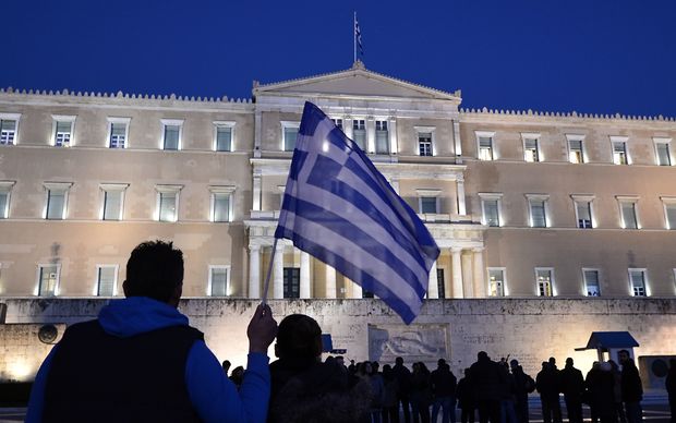 A man holds a Greek flag in front of the Greek parliament in Athens as people gather in support to their government.