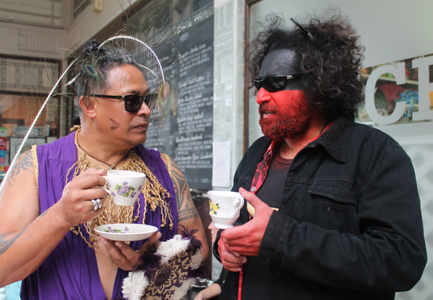 An image of two performers in costume drinking tea.