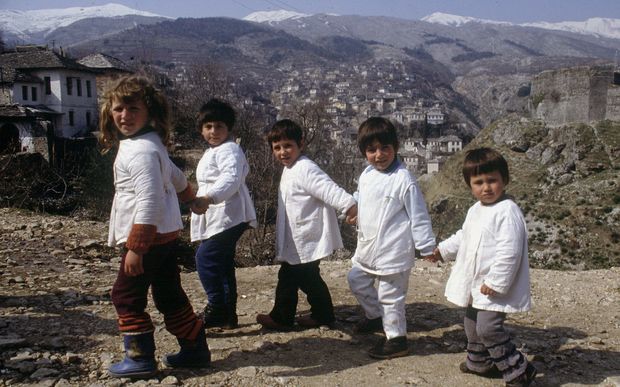 Children in matching while tops at edge of village with stone buildings and snow topped mountains behind