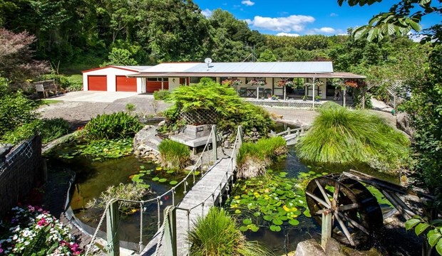 A house with a large pond and a waterwheel in front of it in Kawerau