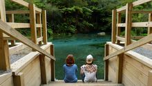 Two young Dutch tourists sit on some wooden steps that lead to the clear blue/green water at Blue Spring, Putaruru