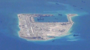 A US Navy surveillance photo of Fiery Cross Reef. There are several ships surrounding the island which itself features numerous buildings and an airstrip.