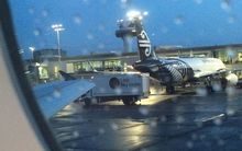 Photo through rain splattered  plane window of  food truck parked at end of Air NZ plane