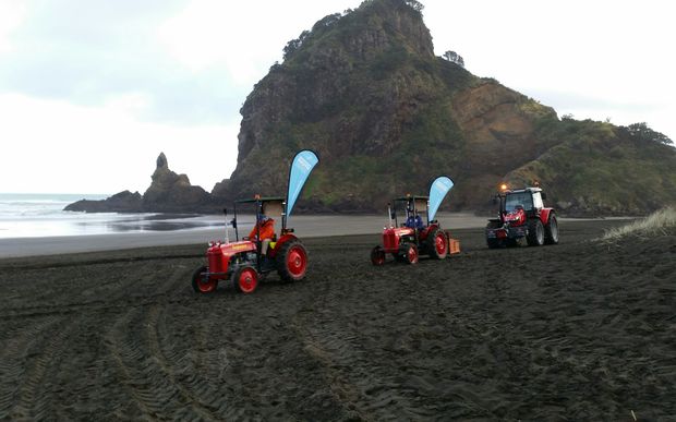 The tractors head off down Piha beach.
