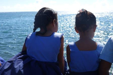 Young schoolgirls sit on the foreshore in Apia