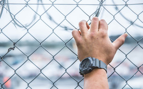 A prisoner's hand against a security fence at Paremoremo.
