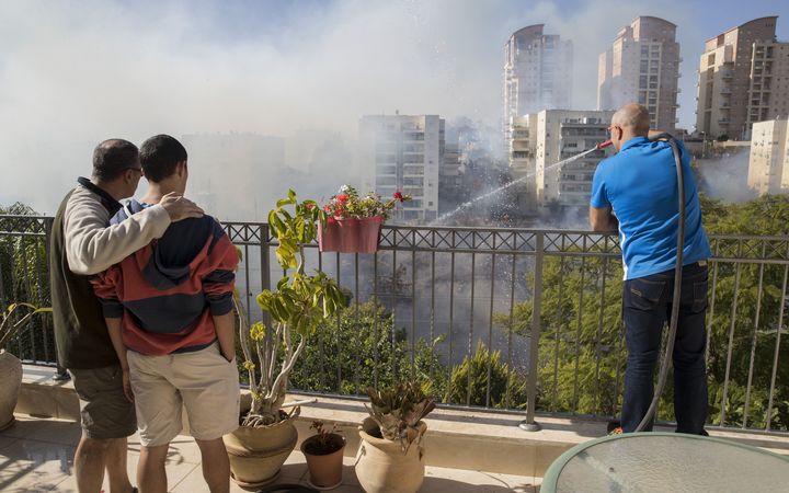 Two Israelis watch as another tries to extinguish a bushfire with a hose from a rooftop in the Israeli city of Haifa.