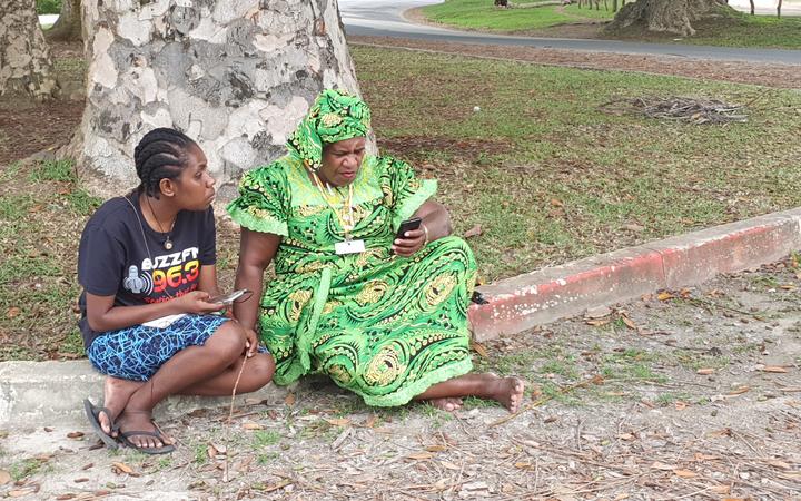 Kizzy Kalsakau, (right), and her colleague wait on the roadside about 1km out from the airport