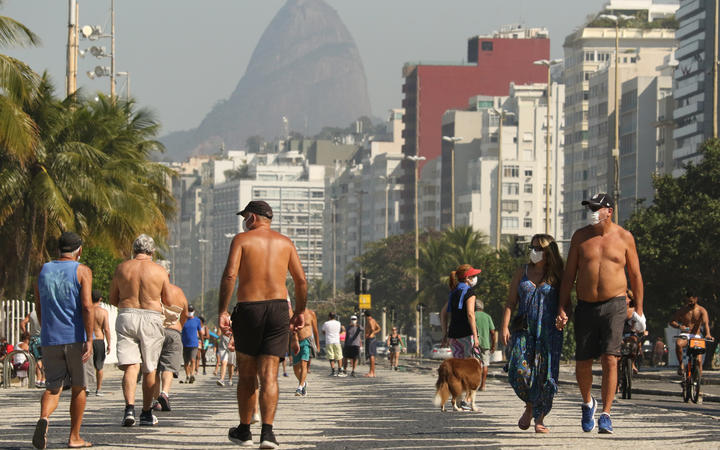 People walk along the edge of Copacabana beach in Rio de Janeiro, Brazil. The country's Covid-19 death toll has surpassed Italy. 