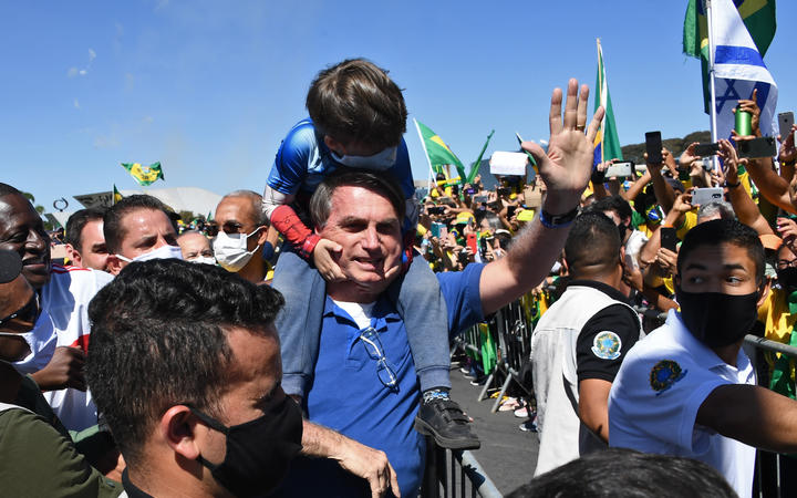 Brazilian President Jair Bolsonaro carries the son of a supporter on his shoulders as he greets supporters during a demonstration in Brasilia, during the Covid-19 coronavirus pandemic on May 31, 2020.
