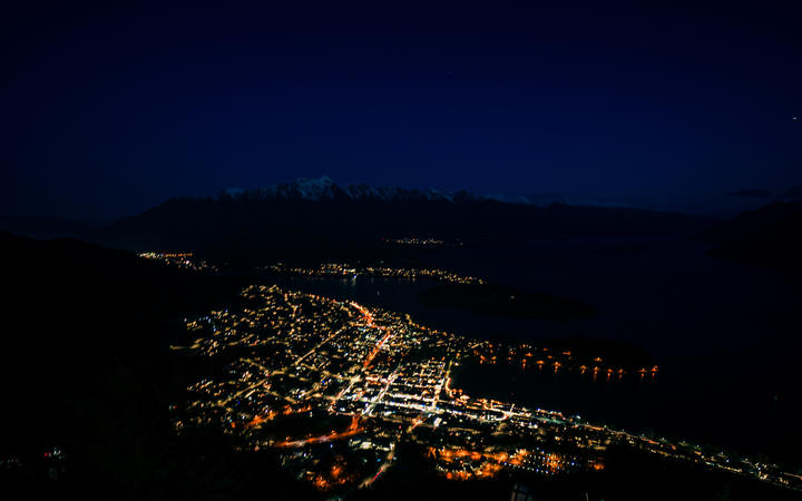 Beautiful night view of Queenstown with the snow capped mountains in the background taken during an orange sunset from the Queenstown, New Zealand Skyline