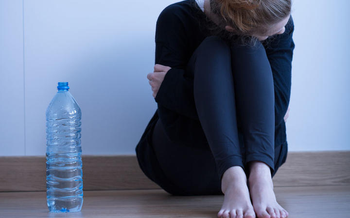 Photo of a sad looking anorexic girl with a water bottle next to her