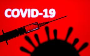Coronavirus model and medical syringe are seen with 'covid-19' sign displayed on a screen in the background in this illustration photo taken in Poland on June 9, 2020. 