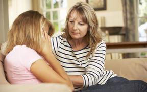 Mother Comforting Teenage Daughter Sitting On Sofa At Home