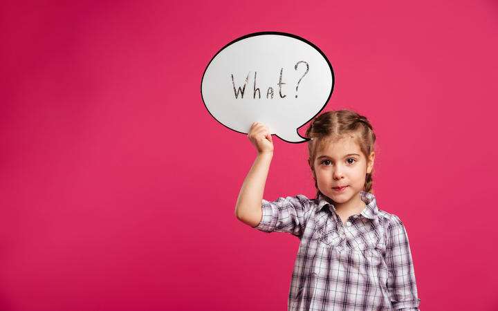 Image of pretty little girl child standing isolated over pink background. Looking camera holding speech bubble.
