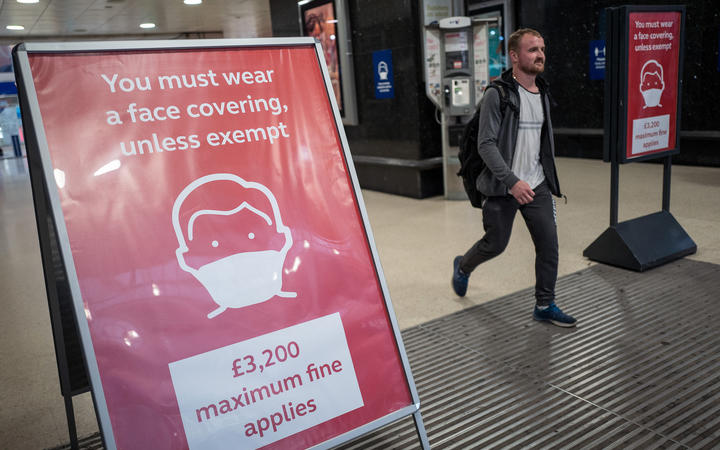 A man, not wearing a face covering, passes signs telling travellers they must wear face mask unless they are exempt, as he leaves Victoria station during the evening 'rush hour' in central London on September 23, 2020. - 
