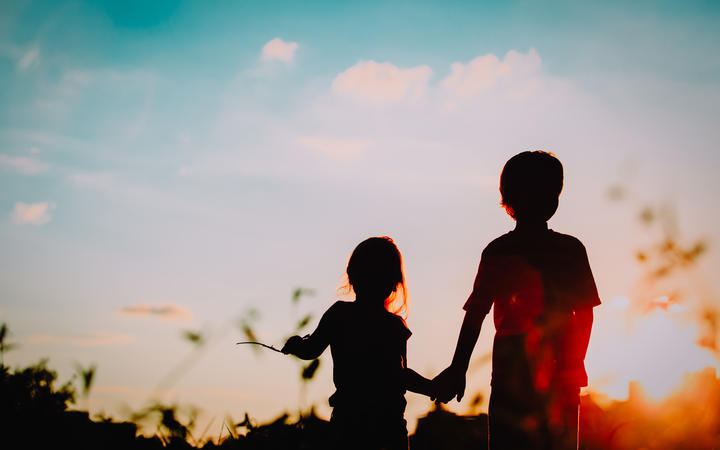 little boy and girl silhouettes holding hands at sunset nature