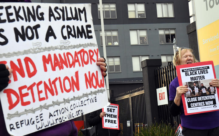 People hold up placards during a pro-refugee rights protest in Melbourne on June 13, 2020 as several asylum seekers who were evacuated for medical reasons from offshore detention centres on Nauru and Manus Island, look down from the hotel where they have been detained. 