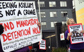 People hold up placards during a pro-refugee rights protest in Melbourne on June 13, 2020 as several asylum seekers who were evacuated for medical reasons from offshore detention centres on Nauru and Manus Island, look down from the hotel where they have been detained. 