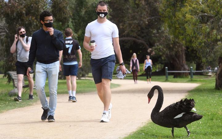 People walk past a swan around Melbourne's Albert Park Lake, 12 October 2020.