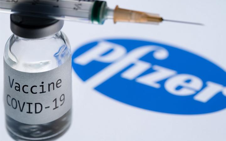 File: This illustration picture taken in Paris on November 23, 2020 shows a syringe and a bottle reading "Covid-19 Vaccine" next to the Pfizer company logo.